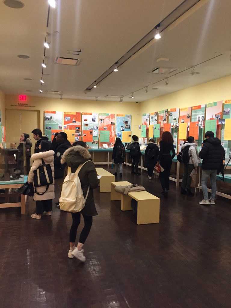 Students walking through museum or poster sessions with posters and exhibits to either side of a large room.