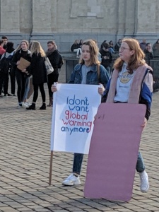 Two teens standing in a square, one of their signs says "I don't want global warming anymore"