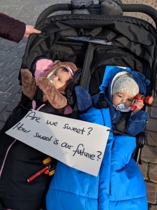 Two children in a stroller with a sign across them that says "Are we sweet? How sweet is our future?"